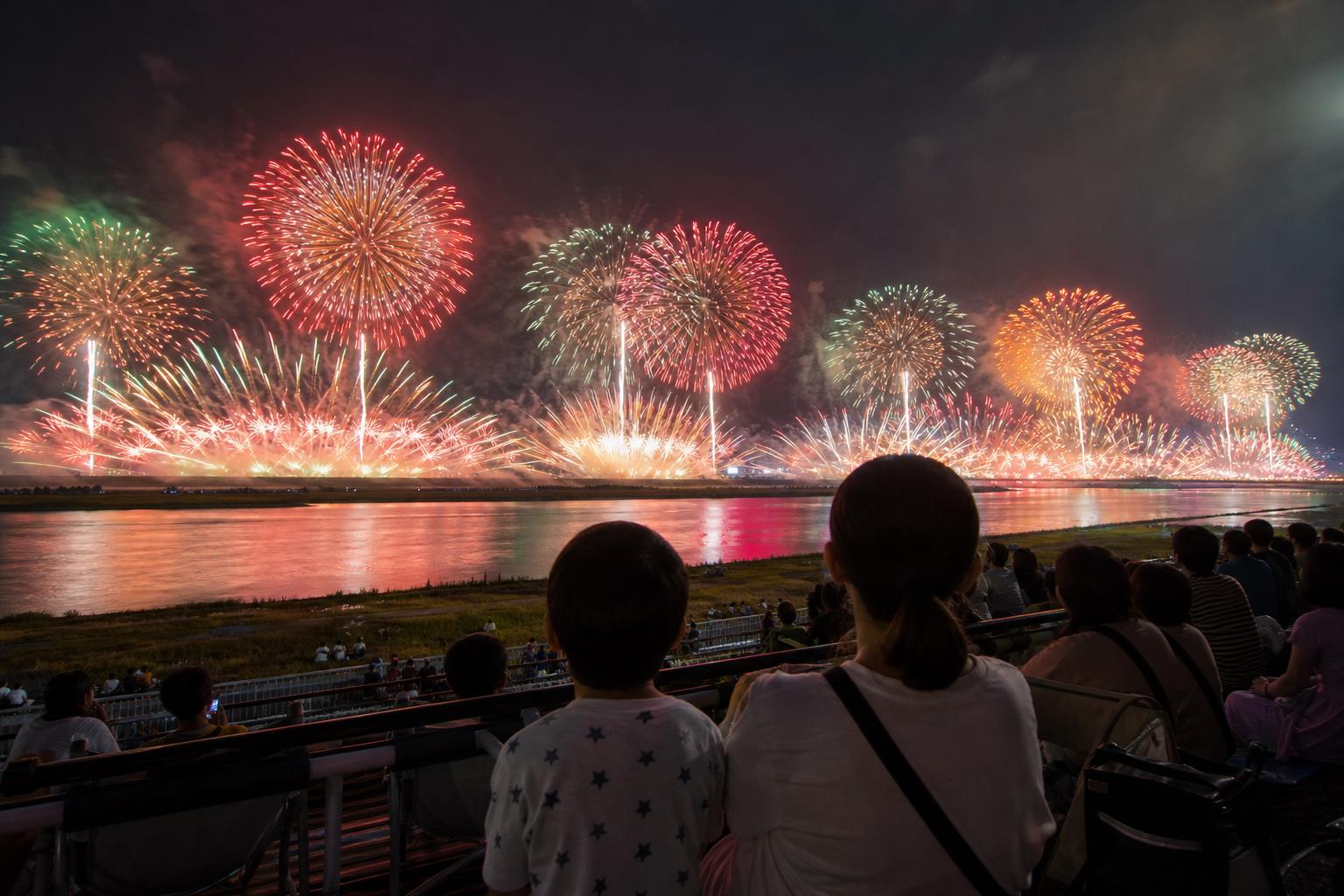 荒川の両岸に広がる大規模な花火を眺める親子